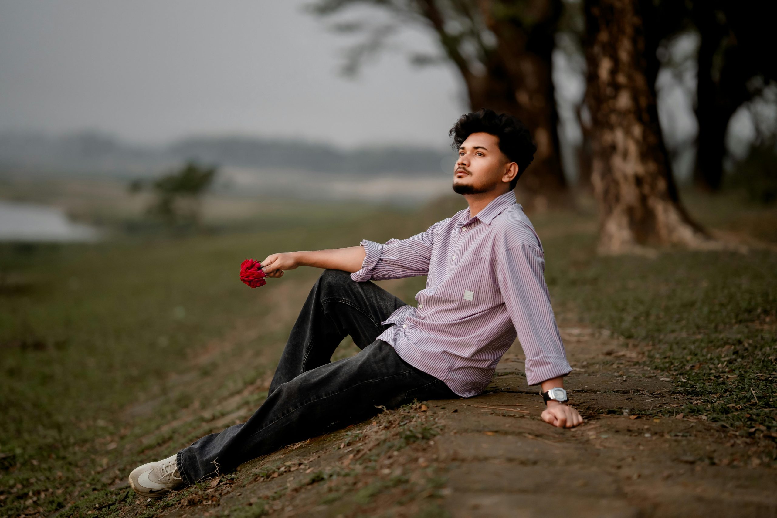 A thoughtful man sits outside holding a flower, exuding a peaceful vibe in Bangladesh.